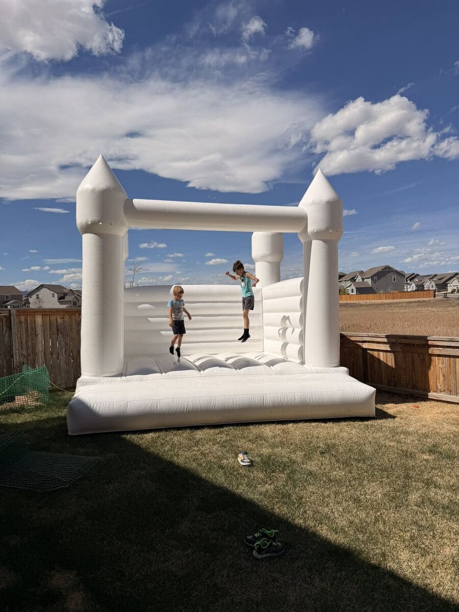 Kids bouncing in a white wedding-style bounce house under a Colorado blue sky