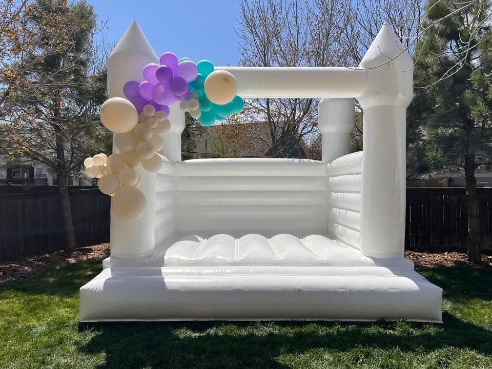 Elegant white bounce house with purple and teal balloon garland