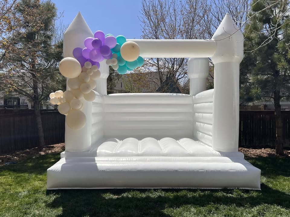 Elegant white bounce house with purple and teal balloon garland